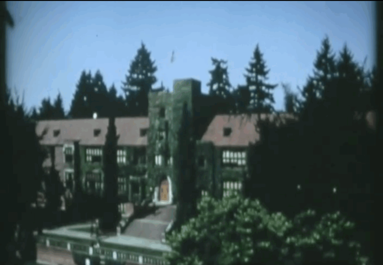 The ivy-covered brick façade of a University of Puget Sound building seen from a distance, framed by trees and a clear sky.